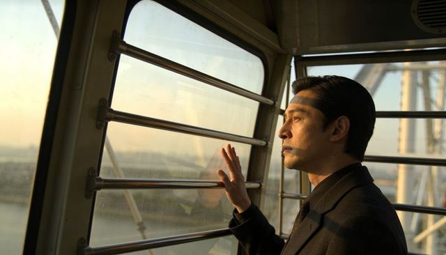 Asian man gazing through ferris wheel cabin at golden hour waterfront, contemplative portrait