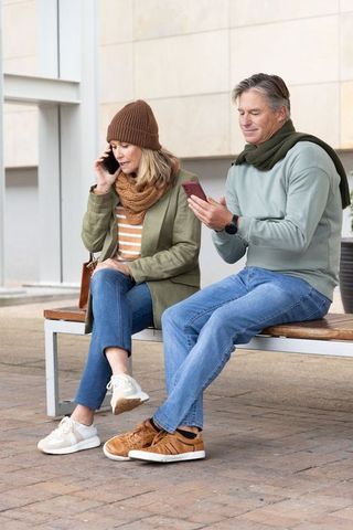 Mature couple sitting on bench, woman talking on phone, man using smartphone, urban plaza