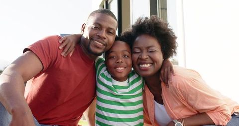 Sunlit african american family smiling and hugging on porch steps — parents and son