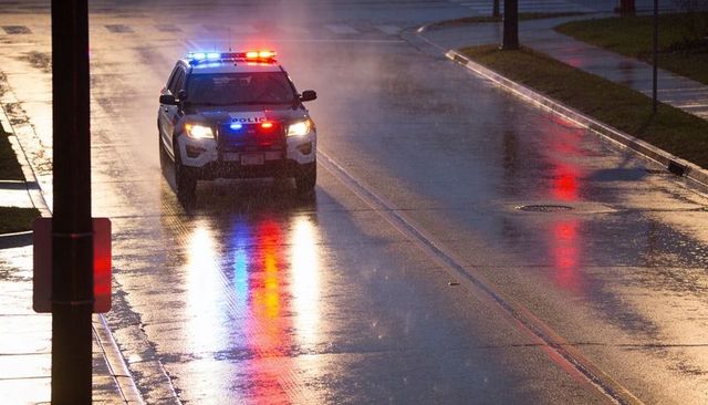 Marked police suv driving on wet city street with red blue roof lights reflecting at night