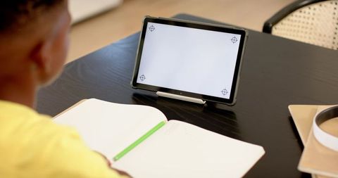 African american child using tablet for remote learning at home desk with open notebook