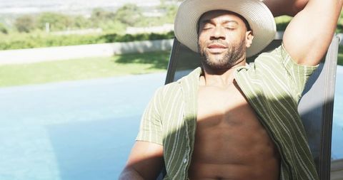 Relaxing poolside recline: man wearing open green shirt and wide-brimmed hat lounging
