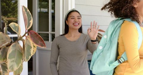 Friendly porch greeting between women smiling host waving goodbye to friend with backpack