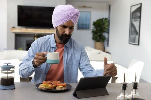Man in Turban Enjoying Breakfast While Working on Tablet at Home