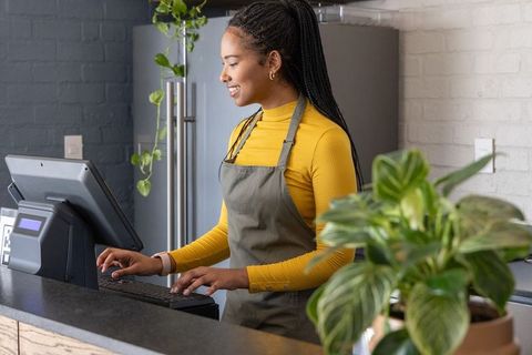 African american barista typing at pos terminal in modern minimalist cafe with plants