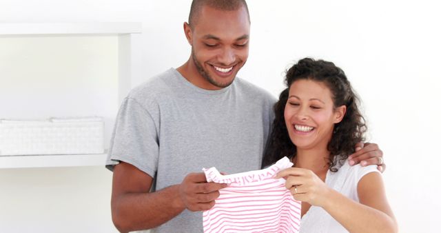 Smiling Couple Holding Baby Clothes in Home Nursery - Download Free Stock Images Pikwizard.com