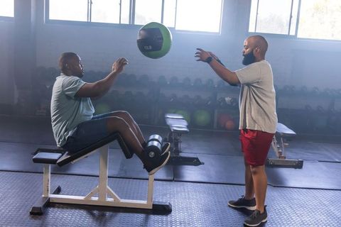 African american trainer coaching client throwing medicine ball on decline bench for core