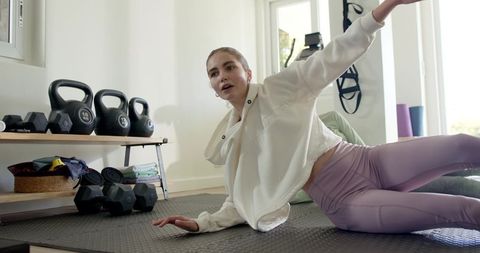 Young woman holding side plank on home workout mat with kettlebells and lavender leggings