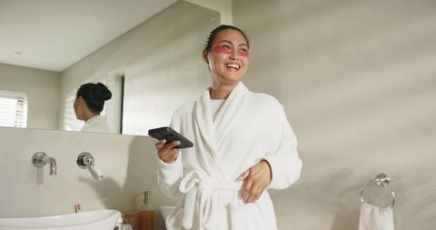 Mid-adult asian woman enjoying skincare routine in beige bathroom wearing white bathrobe