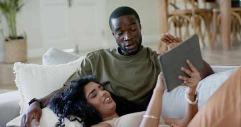 Young couple relaxing on sofa while using tablet for digital research and animated ui demo