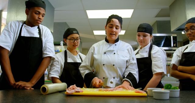 Students in a culinary class receiving hands-on training from a chef. Useful for illustrating cooking courses, training programs, kitchen teamwork, and skill development in the culinary arts.