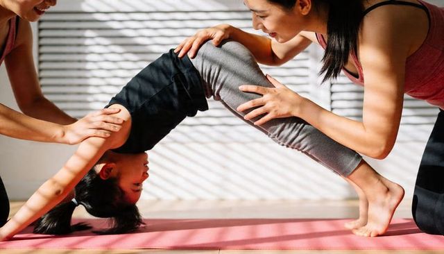 Child practicing supported backbend with instructor guidance on pink yoga mat, sunlit studio