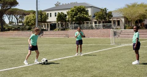 Multicultural teen girls playing soccer on school turf practicing dribbling and teamwork