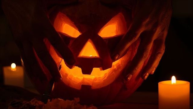 Cradling hands framing glowing jack-o'-lantern with candlelight and pumpkin carving debris