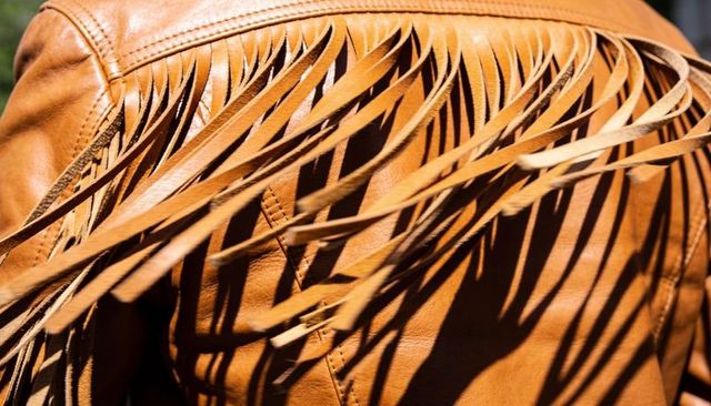 Sunlit cognac leather jacket with long fringe casting dramatic shadows