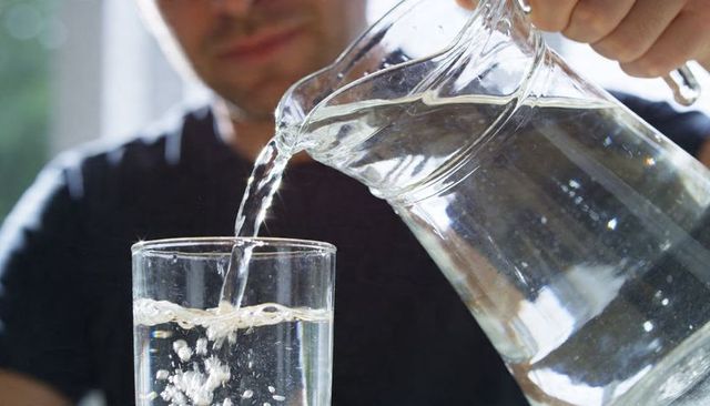 Man pouring water from glass pitcher into tall glass closeup backlit splash for hydration