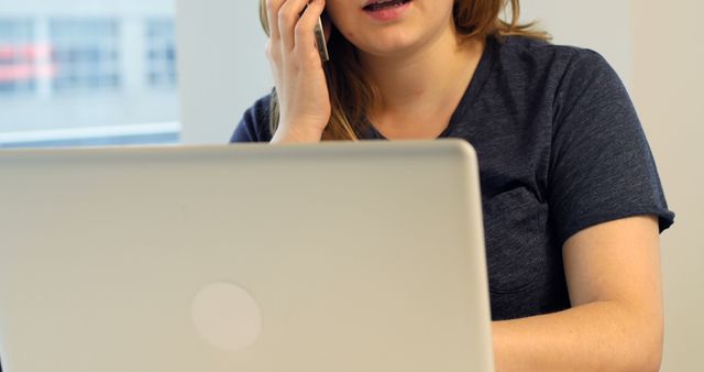 Woman using laptop while talking on mobile phone at home