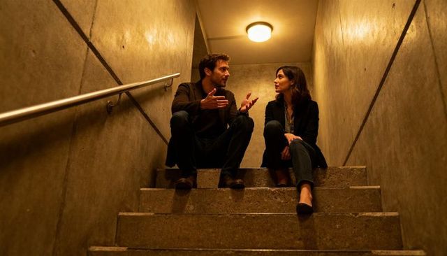 Couple conversing on concrete stairwell wearing blazers and jeans in moody urban scene