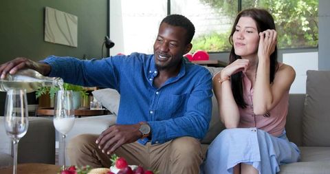 Couple pouring drink on sofa enjoying casual home gathering with strawberries and daylight