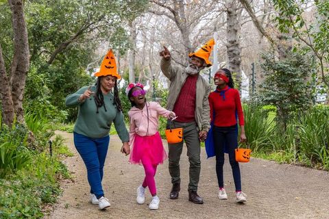African american family walking in park wearing pumpkin hats, carrying halloween buckets