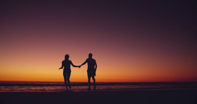 Silhouetted couple enjoys a beach sunset, with copy space. Their romantic walk by the sea creates a serene outdoor setting.