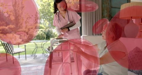 Nurse helping senior woman reaching for walker during home care visit on sunny patio