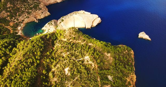 Bird's eye view capturing rugged coastline with lush greenery contrasted against deep blue waters. Ideal for travel blogs, environmental articles, or promotional material for tourist destinations.