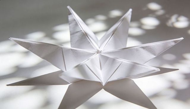 Resting white origami star casting crisp shadows and bokeh highlights on light surface minimalist ge