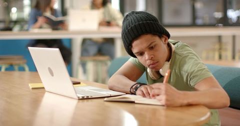 African american student studying at laptop in campus commons writing notes