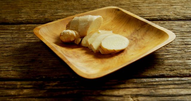 Sliced ginger root is presented on a wooden plate, offering a natural and rustic aesthetic. Ginger is commonly used for its culinary flavors and potential health benefits.