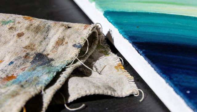 Paint-stained rag beside stretched canvas with blue-green gradient, frayed threads, texture