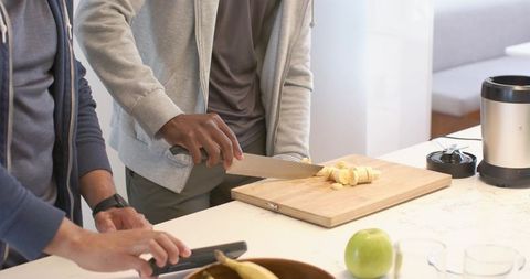 Two people preparing healthy breakfast slicing banana on bright modern kitchen counter