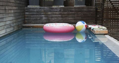 Pink donut float and colorful beach ball floating in outdoor pool with wood privacy panels