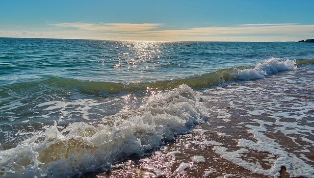 Breaking turquoise wave rolling onto sandy shore with foamy surf and sunlit horizon