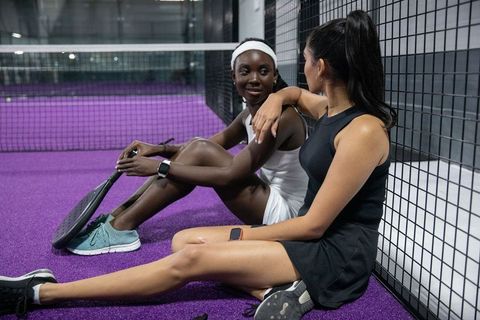 Women athletes sitting on purple padel court talking, resting, sharing team camaraderie
