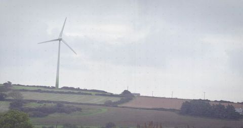 Single wind turbine standing on rural ridge overlooking rolling farmland under cloudy sky