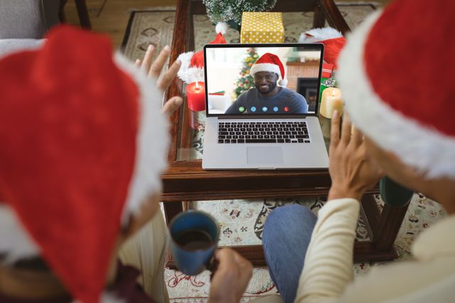 Diverse couple with santa hats having video call with happy african american man. Christmas, celebration and digital composite image.