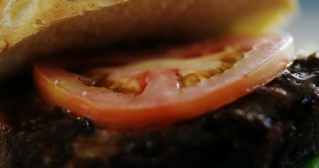 A close-up view of a juicy hamburger with a fresh tomato slice, highlighting the textures and colors of the ingredients. The image captures the appeal of fast food, tempting the viewer with its detailed portrayal of a classic American dish.