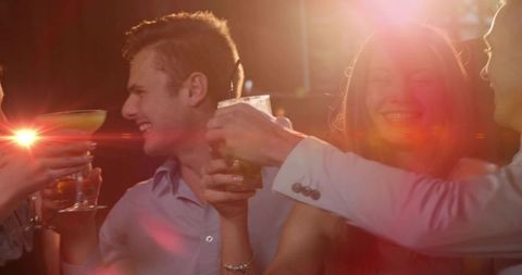 Friends toasting cocktails at lively bar with warm lens flare