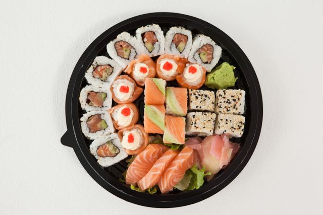 Assorted sushi platter featuring various types of sushi including rolls, sashimi, and nigiri, arranged in a round black box. Ideal for use in food blogs, restaurant menus, culinary websites, or promotional materials for Japanese cuisine.