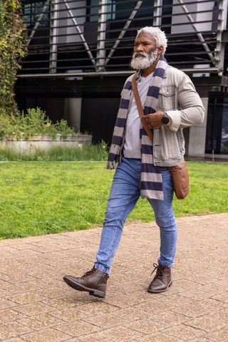 Senior african american man walking along urban path wearing scarf, jacket and satchel