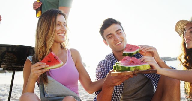A group of friends smiling and eating watermelon during a beach picnic. This cheerful and relaxed image conveys a fun outdoor activity under sunny weather. Ideal for summer campaigns, leisure and lifestyle promotions, or advertisements promoting fresh fruits and outdoor recreational activities.