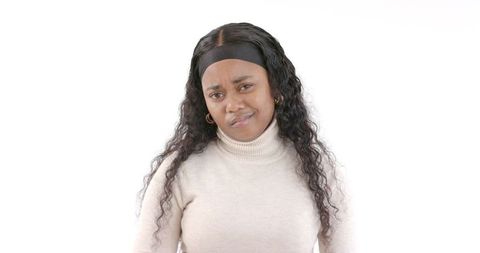 Curly-haired woman in turtleneck conveying confusion on white background