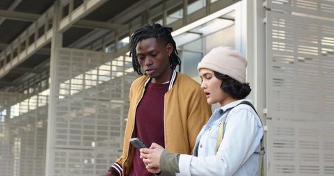 Students checking smartphone at urban bus shelter wearing denim jacket beanie bomber