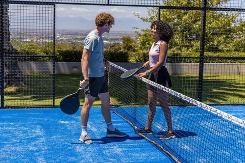 Young couple chatting after padel point on bright blue outdoor court with city skyline