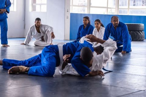 Diverse Martial Arts Class Practicing Grappling Techniques on Gym Mats