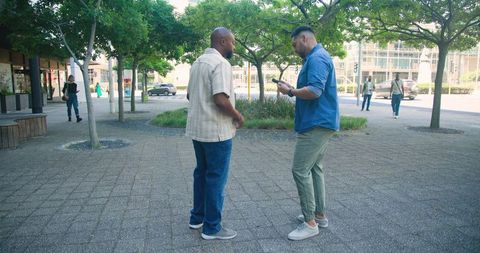 Diverse men conversing in downtown plaza holding smartphone wearing casual shirts urban lifestyle