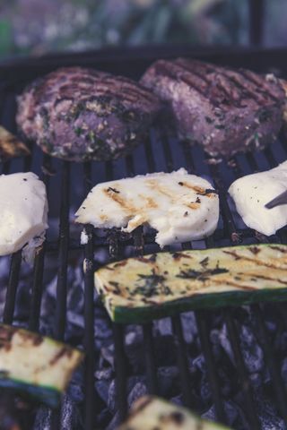Grilling herb-crusted steaks and halloumi with zucchini on charcoal grill rustic bbq