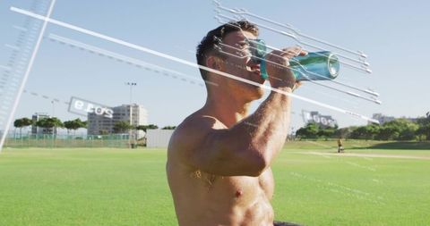 Shirtless male athlete drinking from teal water bottle on sunlit sports field wearing sunglasses
