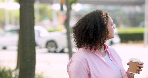 African american woman standing on urban sidewalk holding takeaway coffee cup looking away